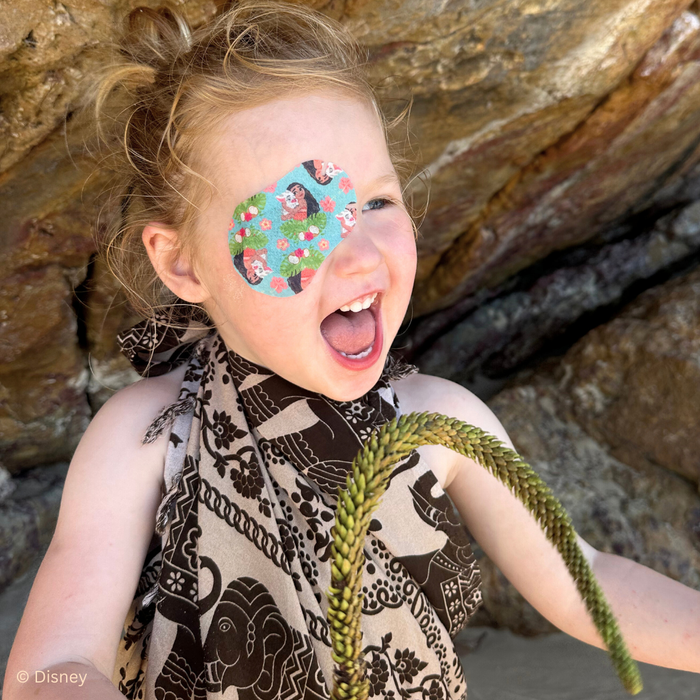 Laughing girl holding a grass stem, wearing a Disney Moana eye patch