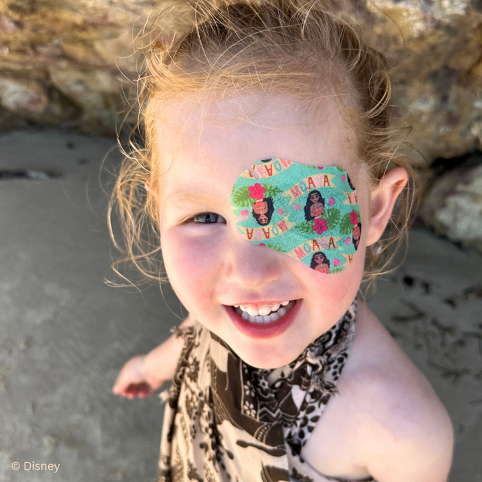 Smiling girl at the beach wearing a teal Disney Moana eye patch