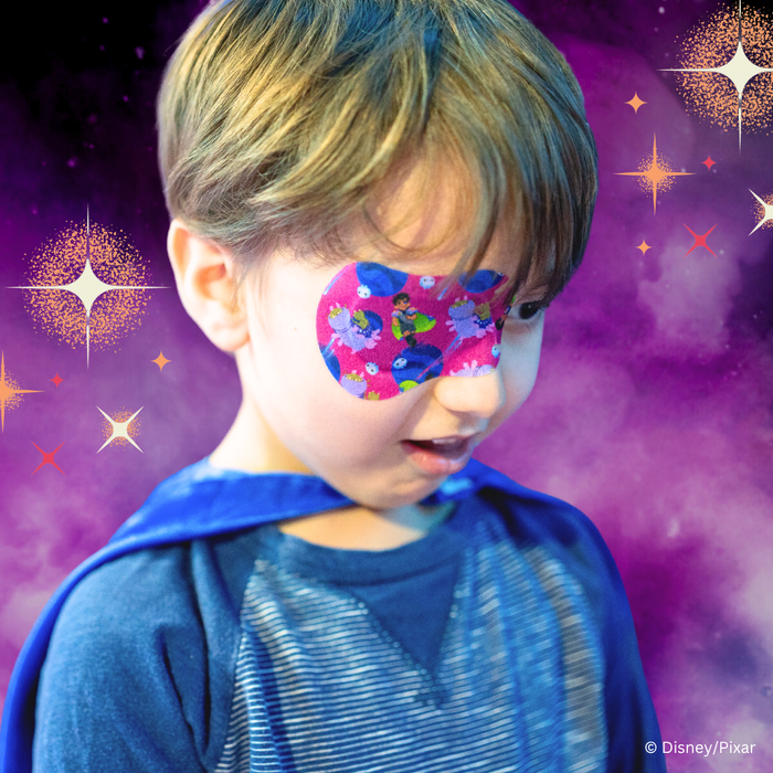 Child in a cape looking down, wearing a pink Elio eye patch