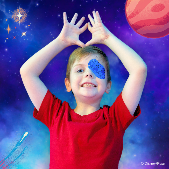 Boy making a heart with his hands, wearing a blue Elio eye patch