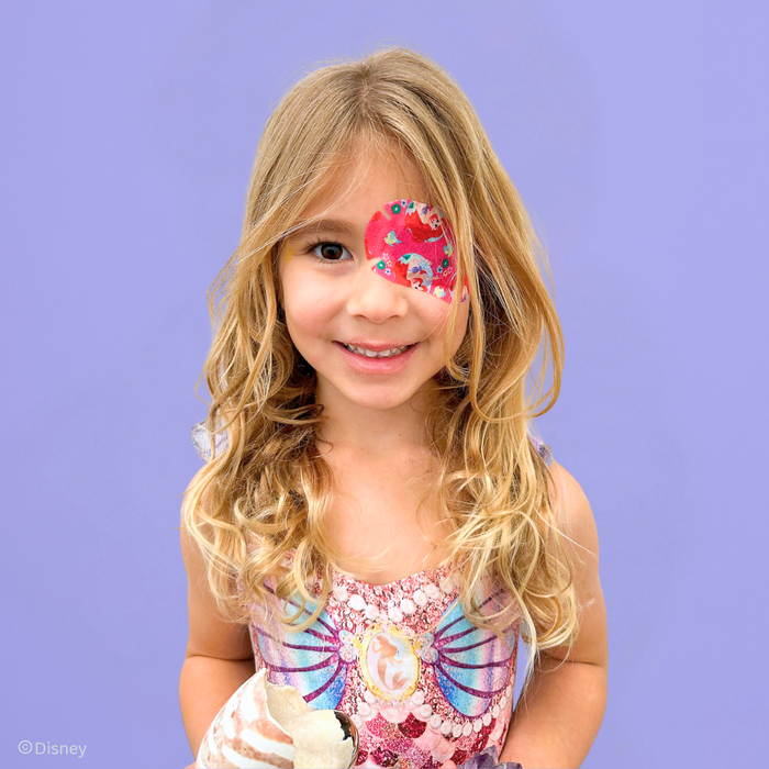 Smiling girl in a mermaid top wearing an Ariel Disney Princess eye patch
