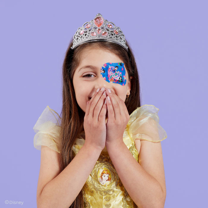 Girl in a Belle dress and tiara covering her smile, wearing a Disney Princess eye patch