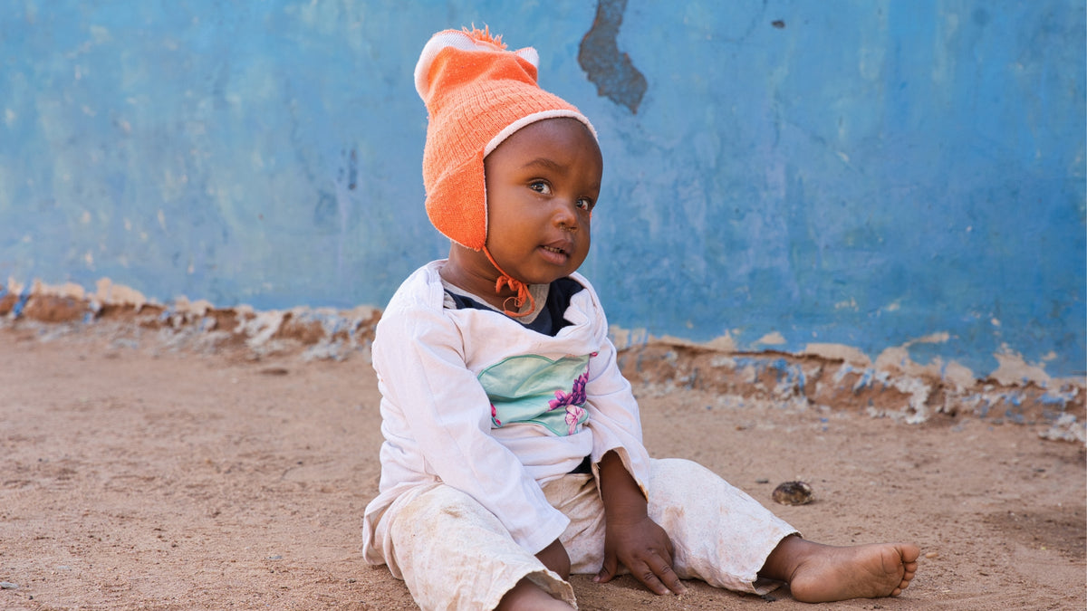 A child sitting outdoors wearing an orange hat